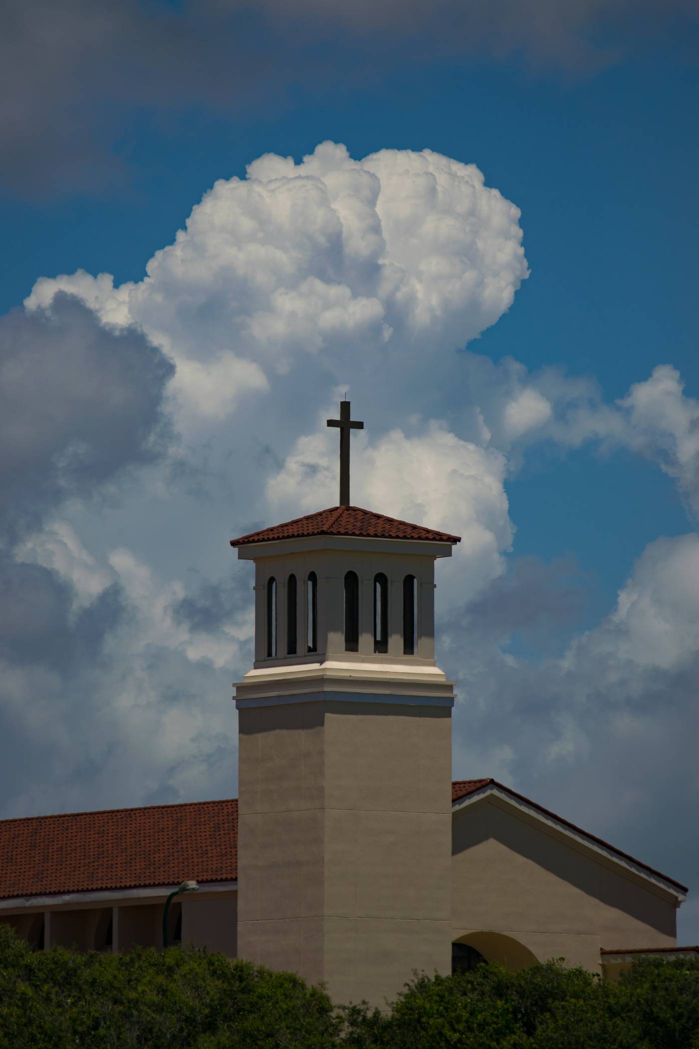 Church bell tower with cross against a dramatic sky and fluffy clouds