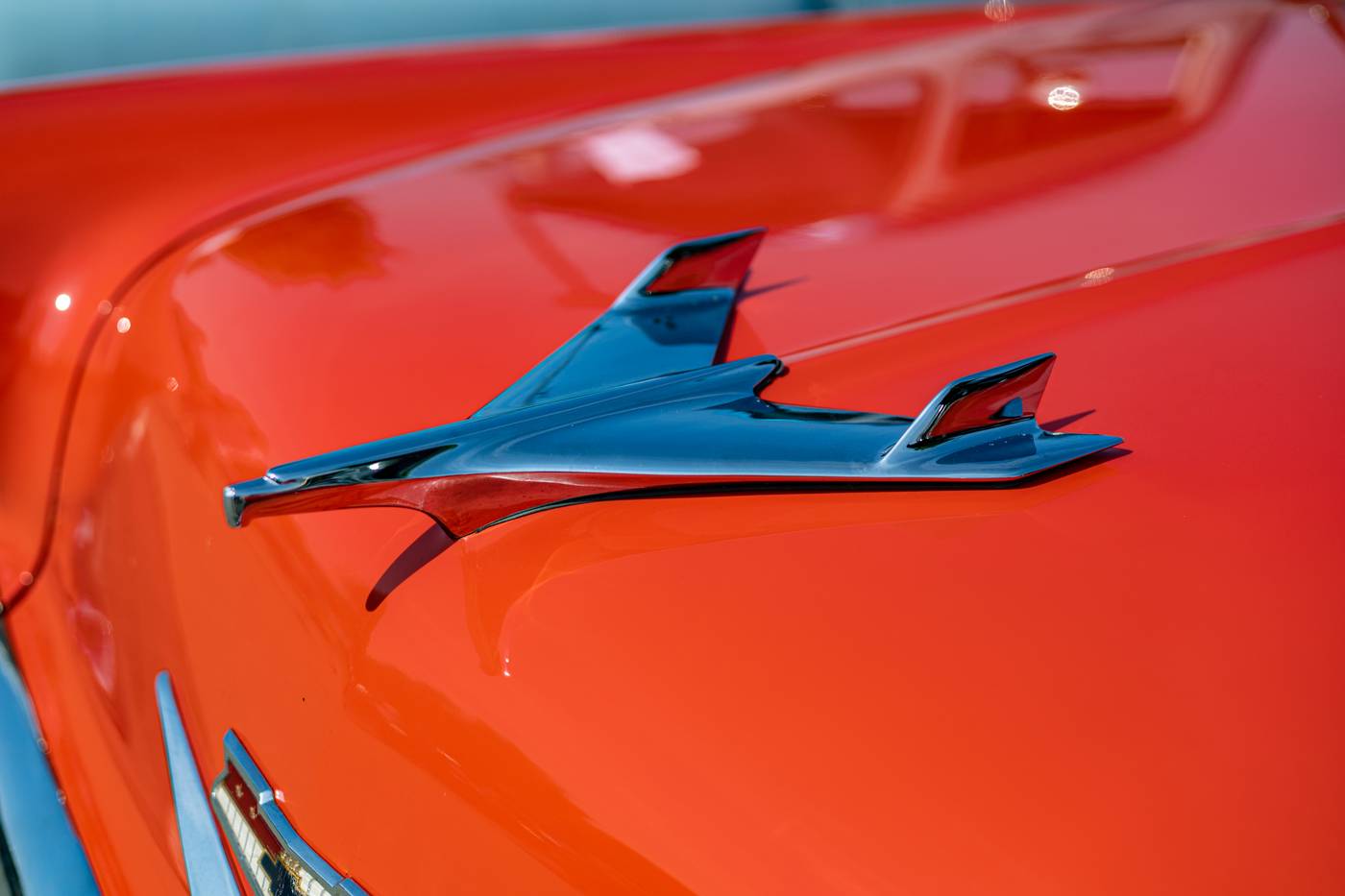 Chrome hood ornament on a shiny orange vintage car under bright sunlight