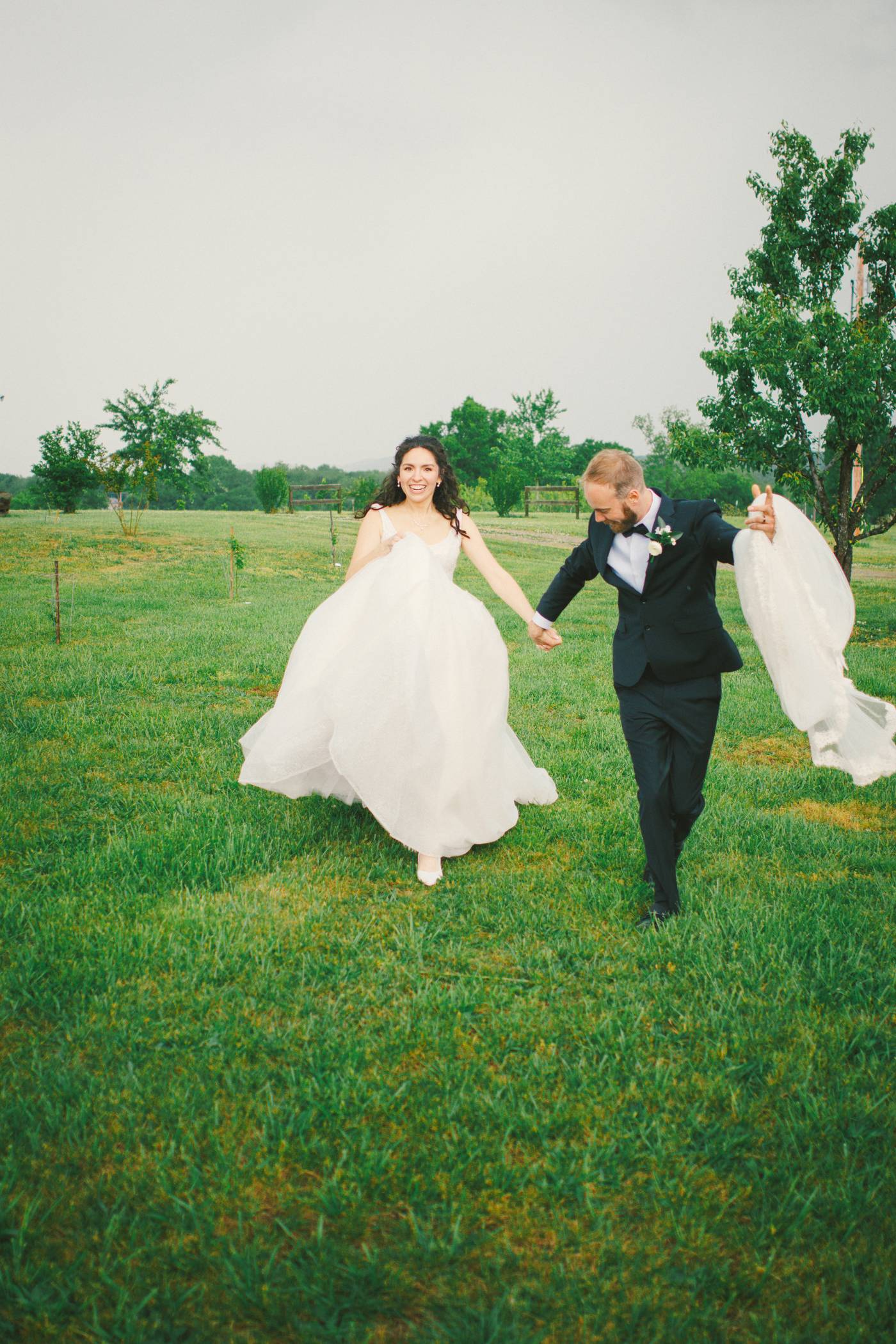 Joyful bride and groom running hand-in-hand across a grassy field during their wedding day
