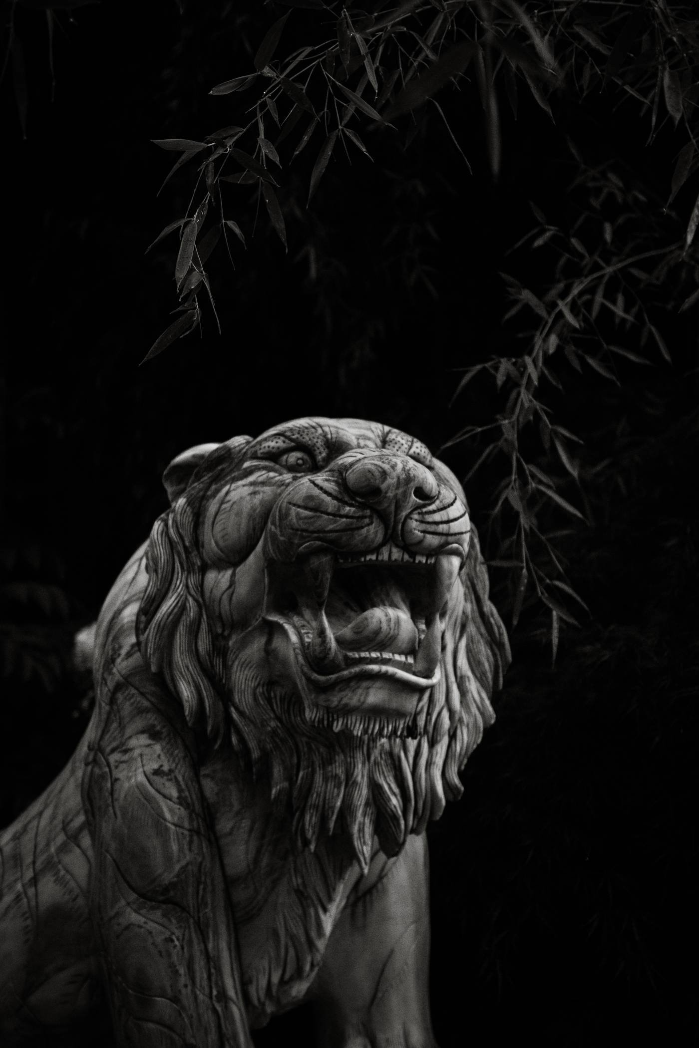 Stone tiger statue with open mouth and bamboo branches against a dark background