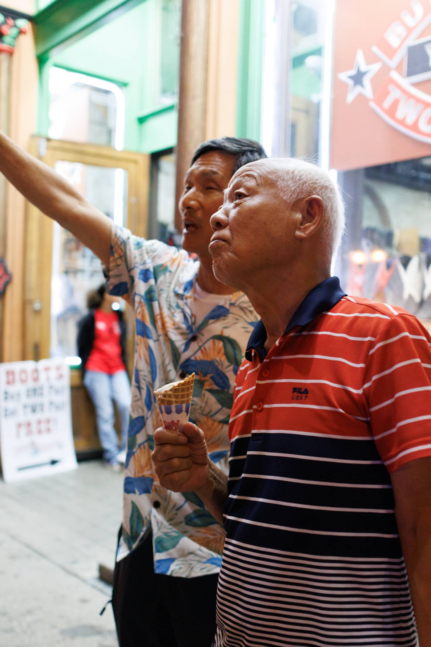 Two men enjoy ice cream on a city street with a blurred background