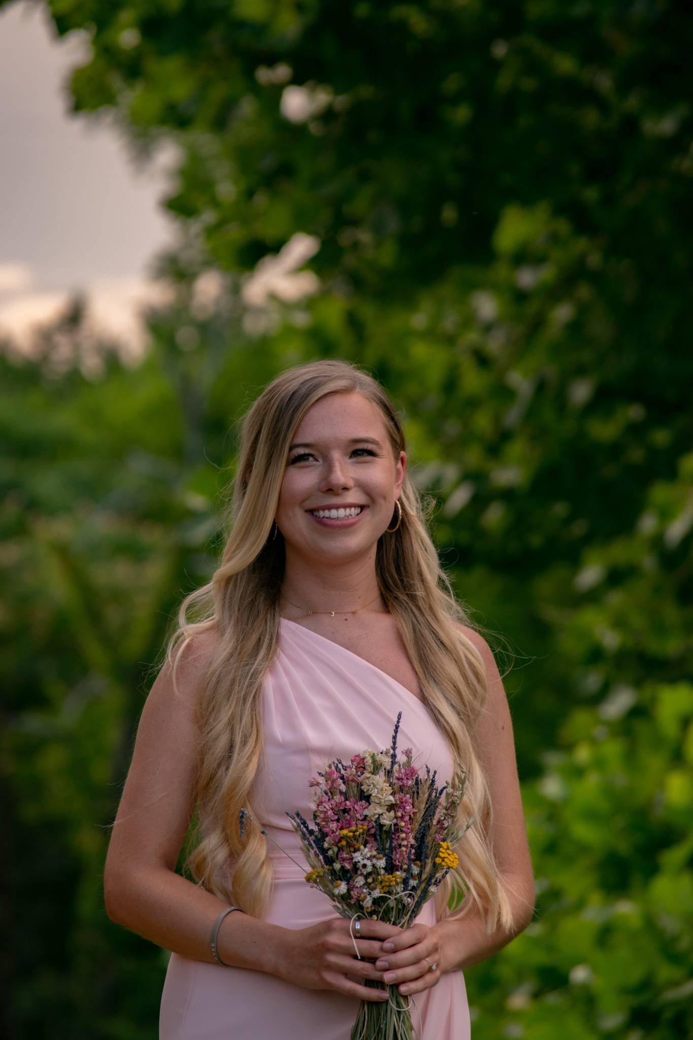 Smiling bridesmaid in a pink dress holding a wildflower bouquet outdoors