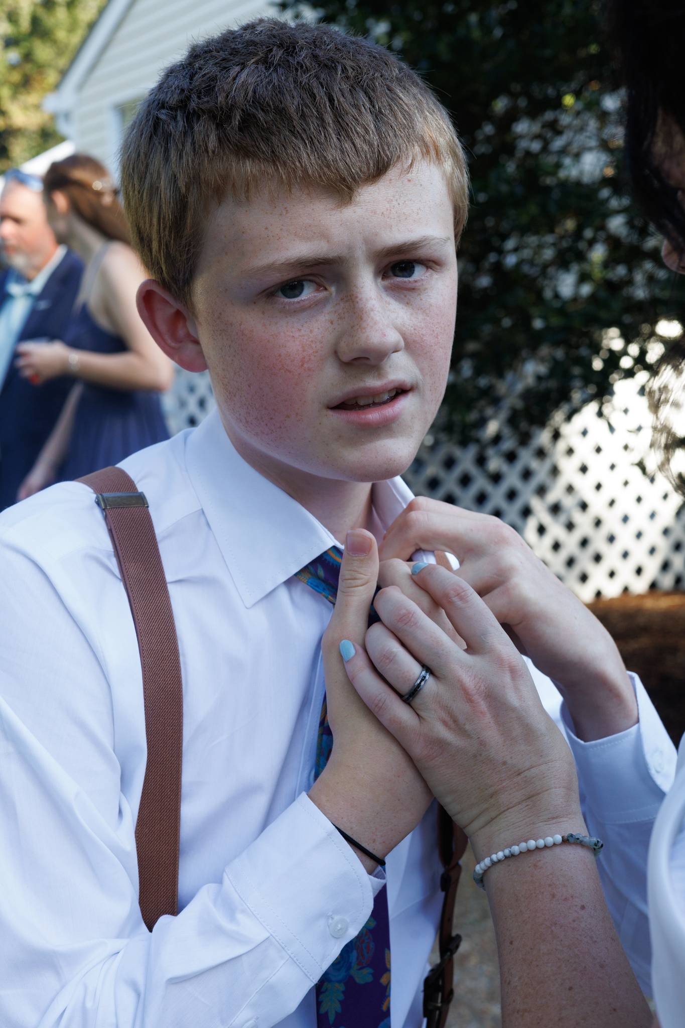 Young groomsman in suspenders gets his collar adjusted before the wedding ceremony
