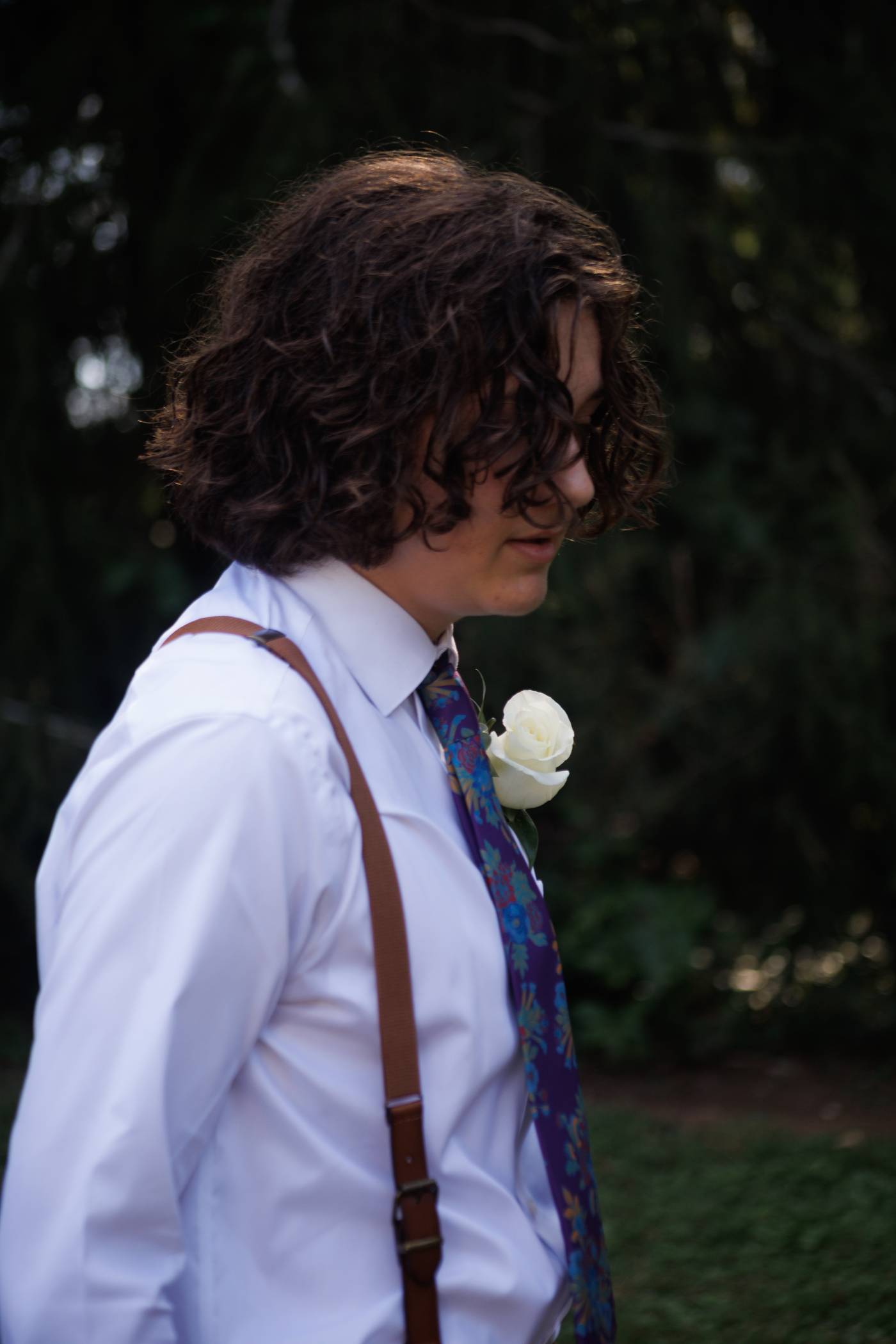 Groomsman with curly hair and a white boutonniere looks down during the wedding