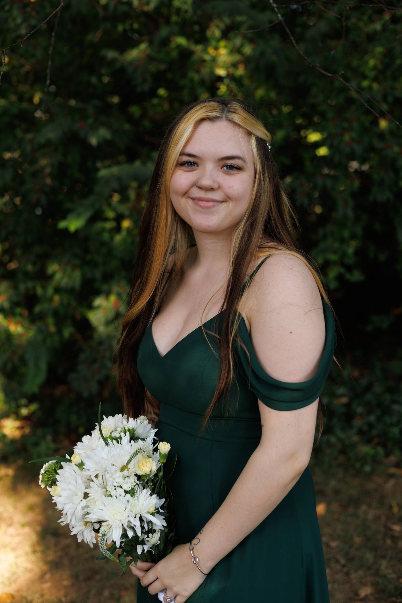 Smiling bridesmaid in a green dress holding a white daisy bouquet