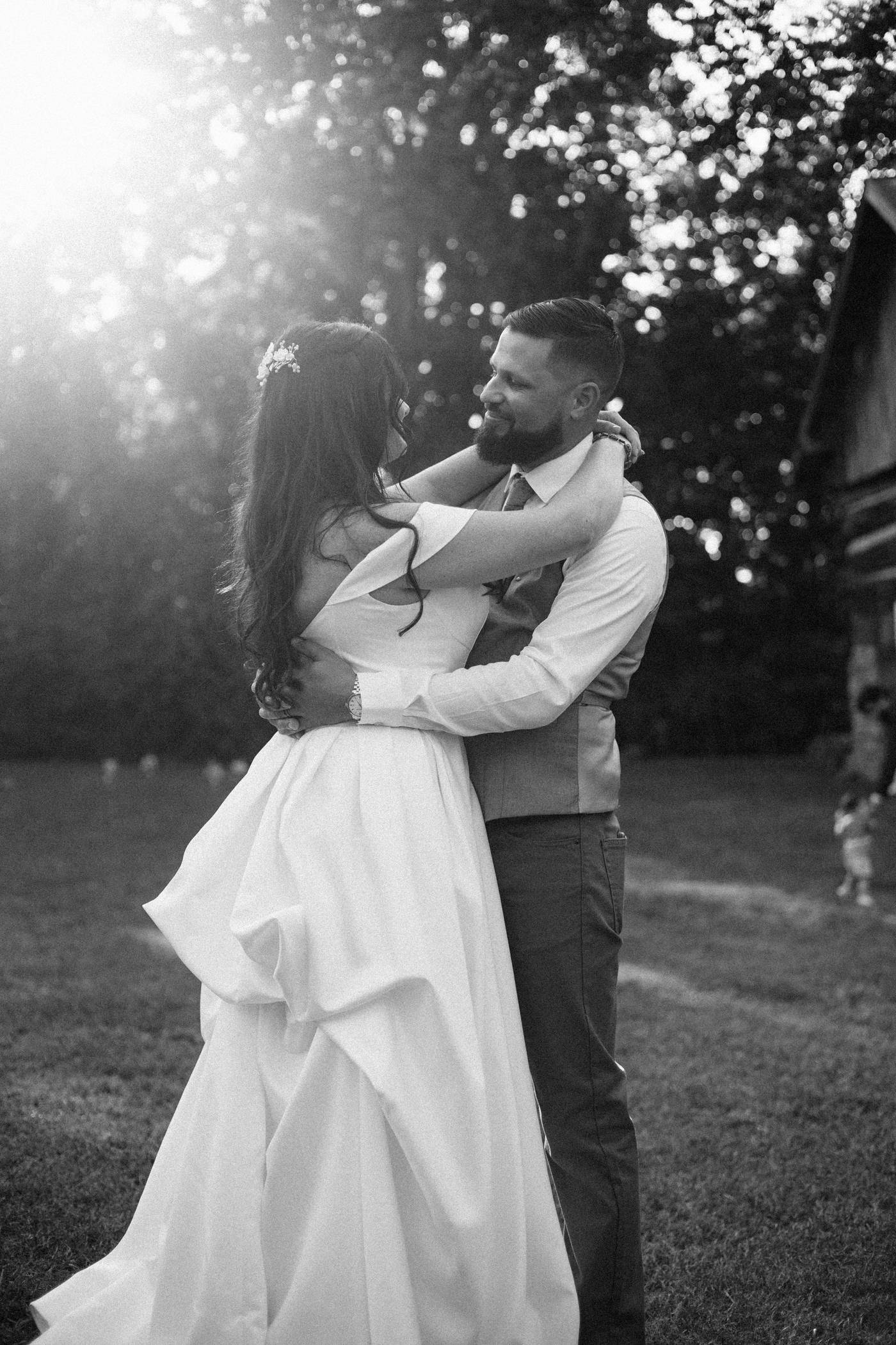 Black and white photo of a bride and groom embracing in backlit trees