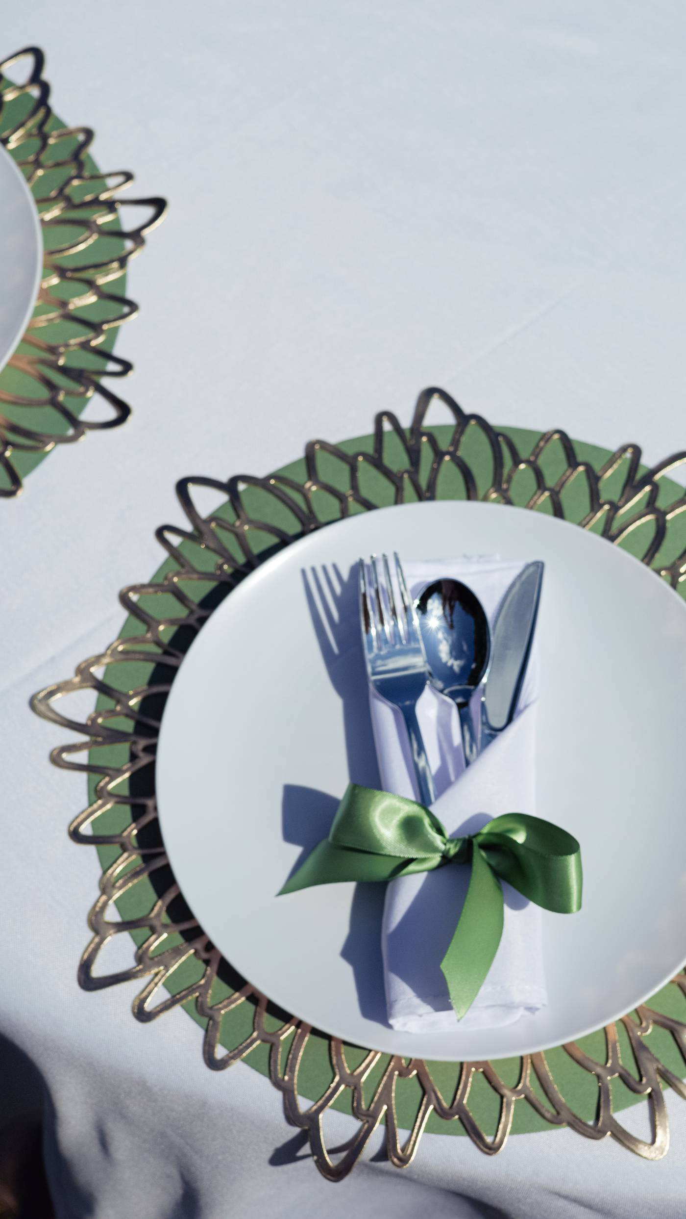 Wedding reception place setting with a gold charger and silverware tied in green ribbon