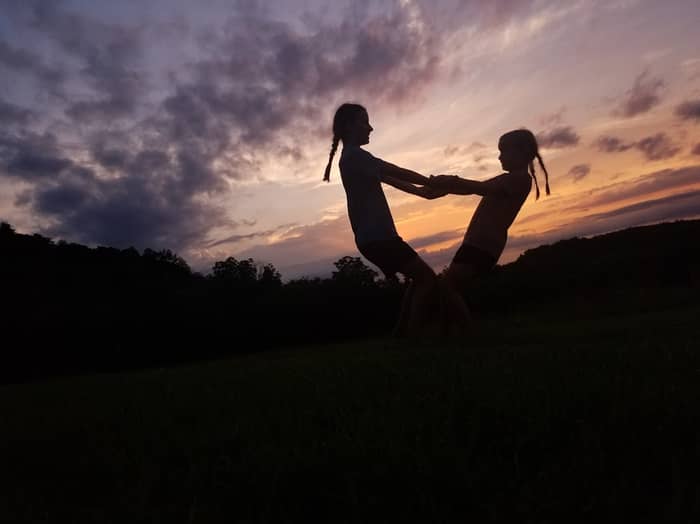 Two girls hold hands playing in a field at sunset