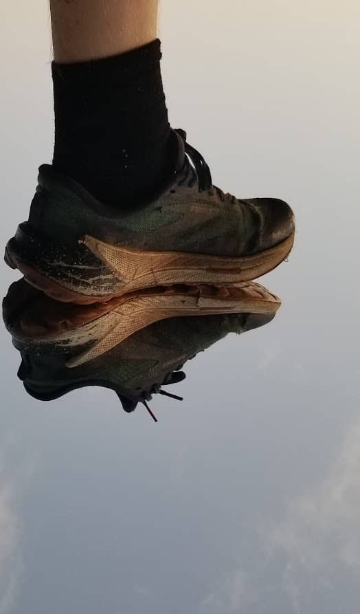 Dirty running shoe reflected on a mirrored surface against a cloudy sky