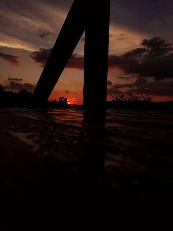 Silhouetted structure against a dramatic sunset over a reflective surface