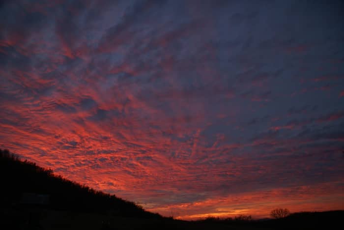 Dramatic red and orange clouds fill the sky at sunset over a dark, silhouetted landscape