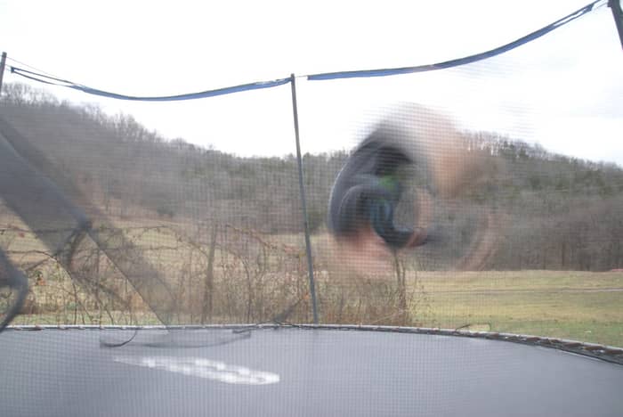 Person performing a flip on a trampoline outdoors with a blurred motion effect