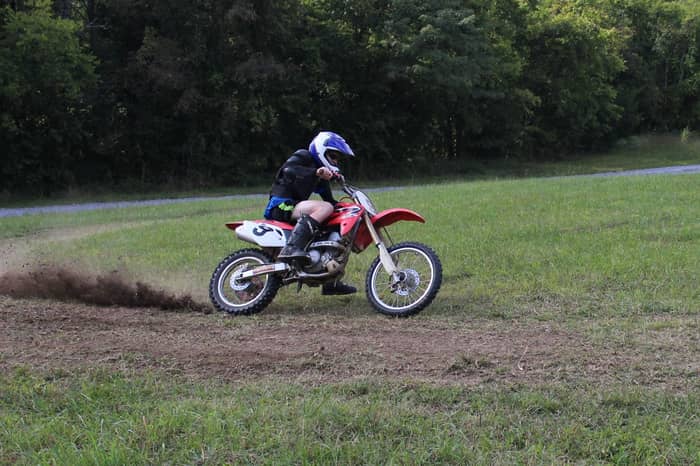 Motocross rider kicks up dirt while turning on a grassy track surrounded by trees