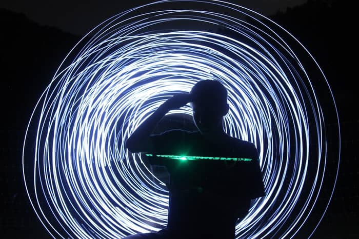 Silhouette of a person against a swirling vortex of white light trails at night