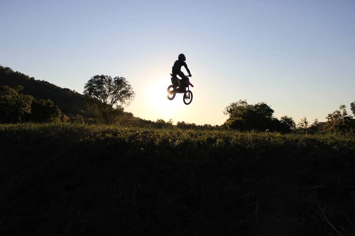 Silhouette of a motocross rider mid-air against a bright sunset sky
