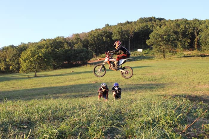 Motocross rider soars through the air above two spectators in a grassy field
