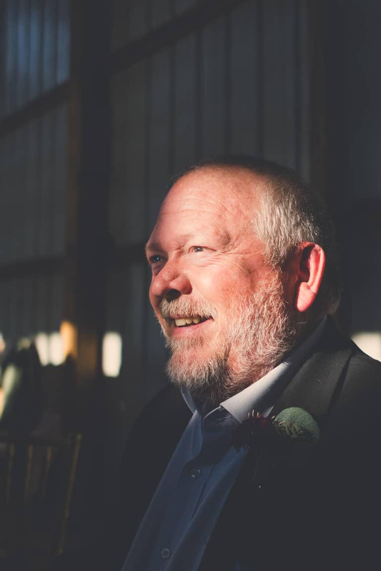 Smiling groom with beard and boutonniere in a dimly lit wedding venue
