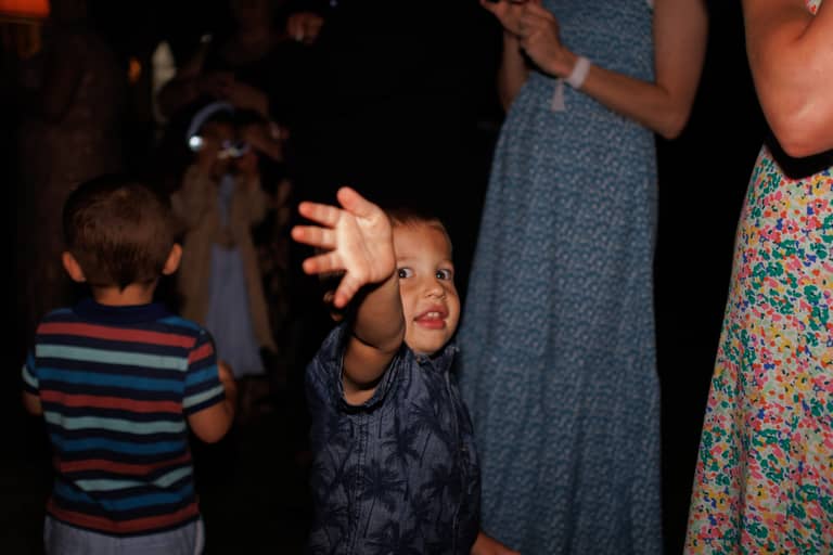 A young boy reaches out at a lively wedding reception with guests in the background