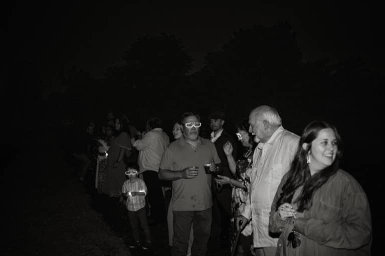 Wedding guests in novelty glasses mingle outdoors at night with a festive mood