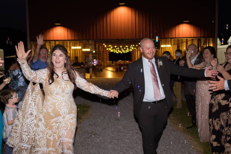 Joyful wedding couple walks through bubbles outside a barn reception venue