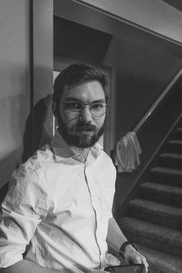 Groom with glasses and beard looks seriously at the camera in a candid wedding moment