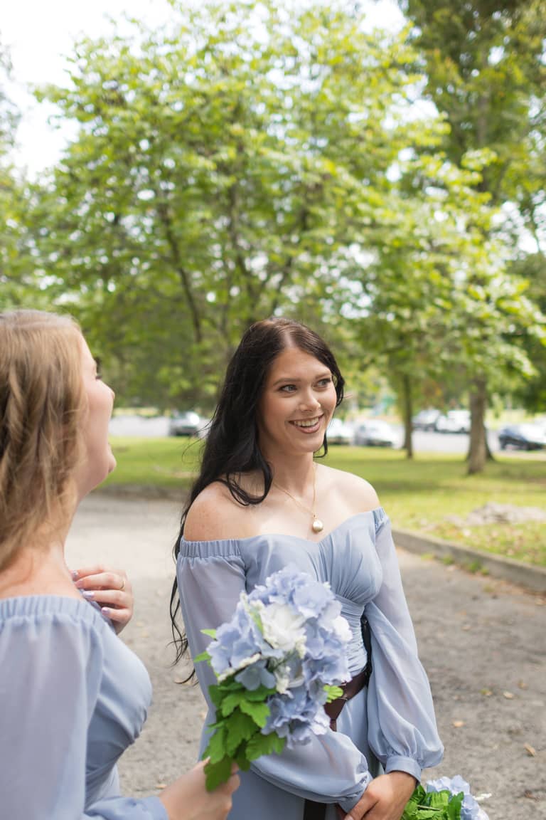 Two bridesmaids in blue dresses laugh outdoors holding bouquets at a wedding