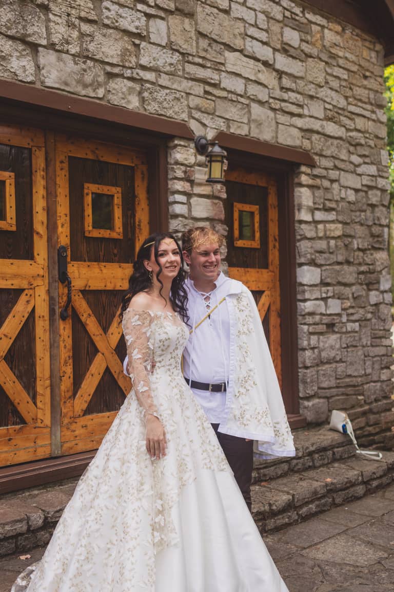 Joyful bride and groom pose in front of rustic wooden doors and stone building during wedding