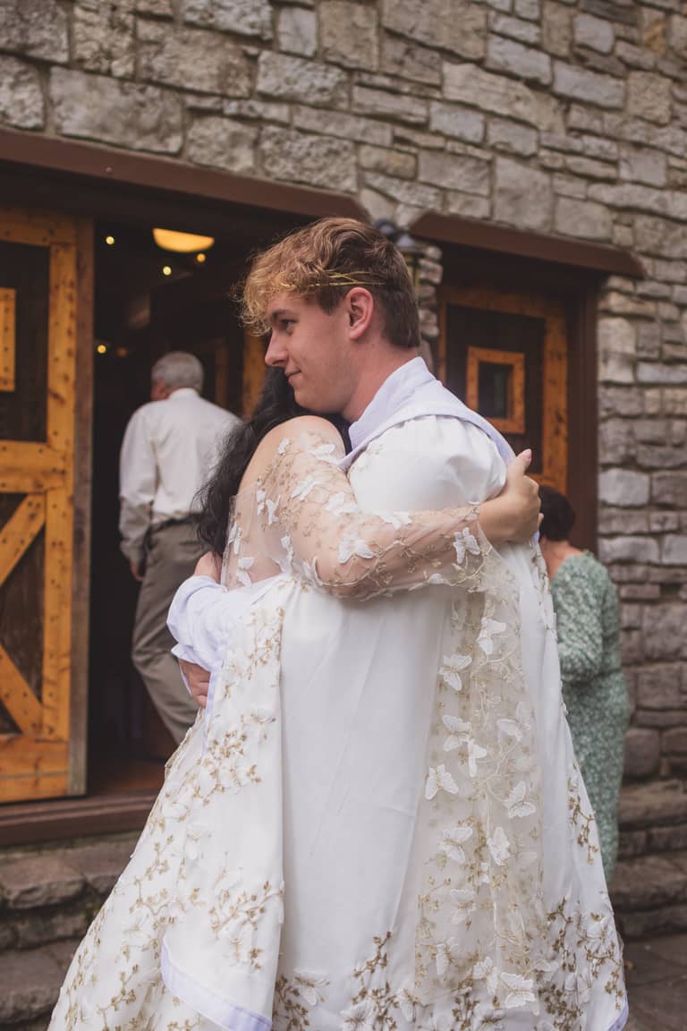 Bride and groom embrace outside stone building during wedding ceremony