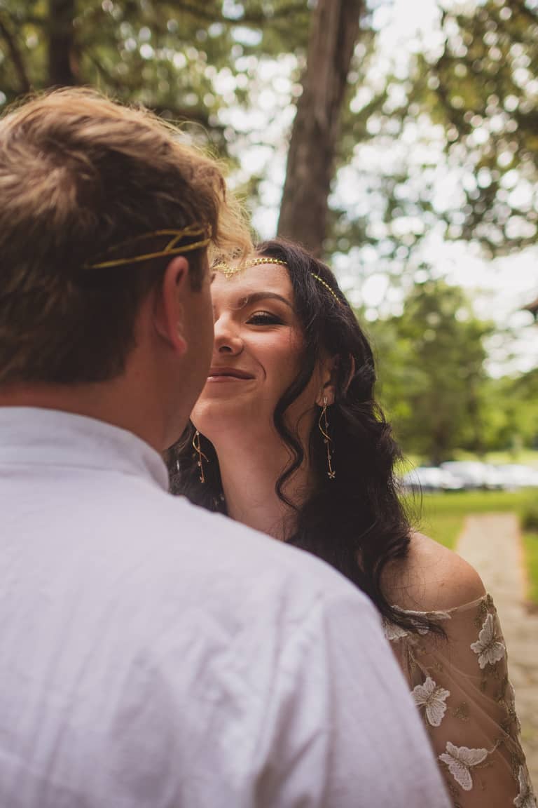Bride smiles at groom during an intimate outdoor wedding ceremony surrounded by trees