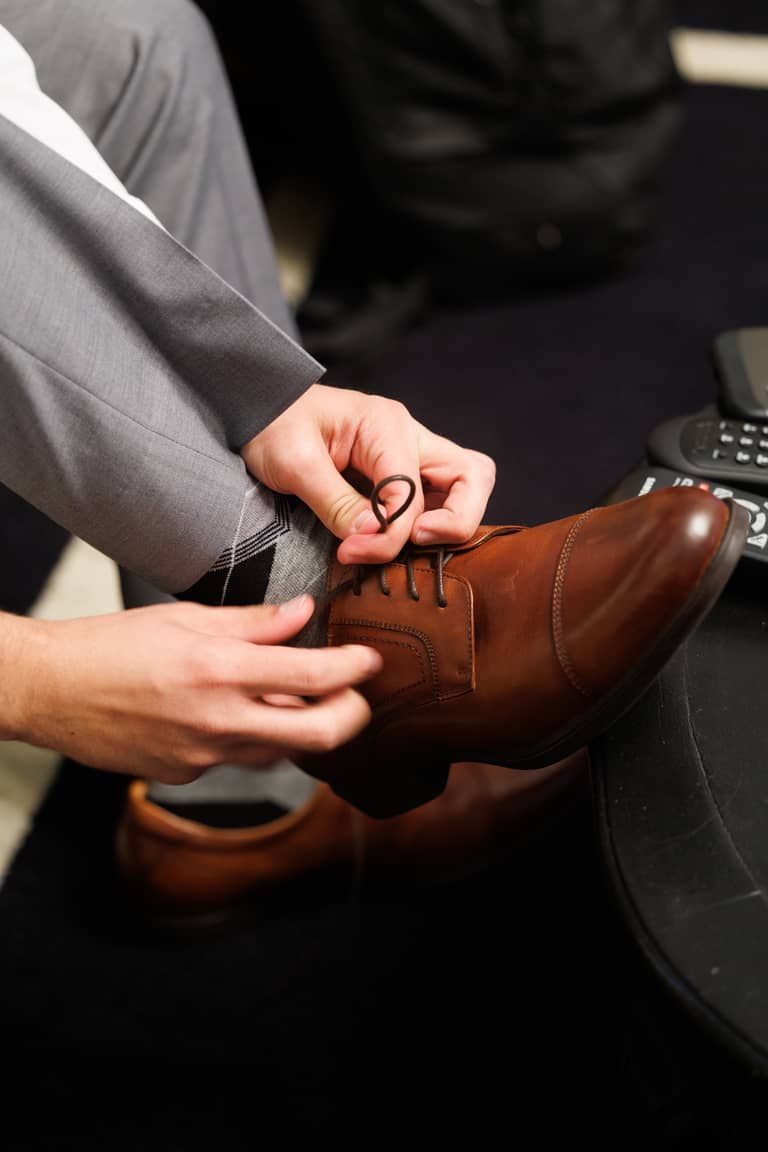 Groom tying his brown dress shoe laces during a wedding preparation