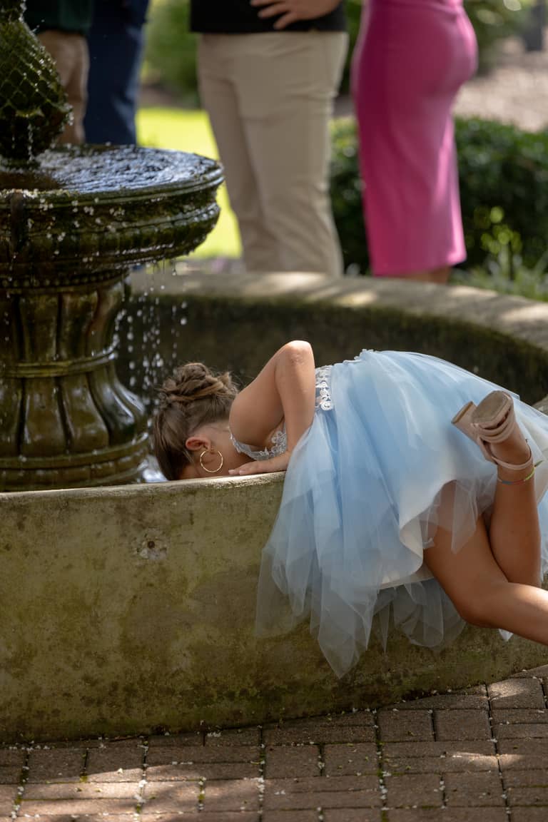 Flower girl in blue dress drinks from a mossy fountain at a wedding