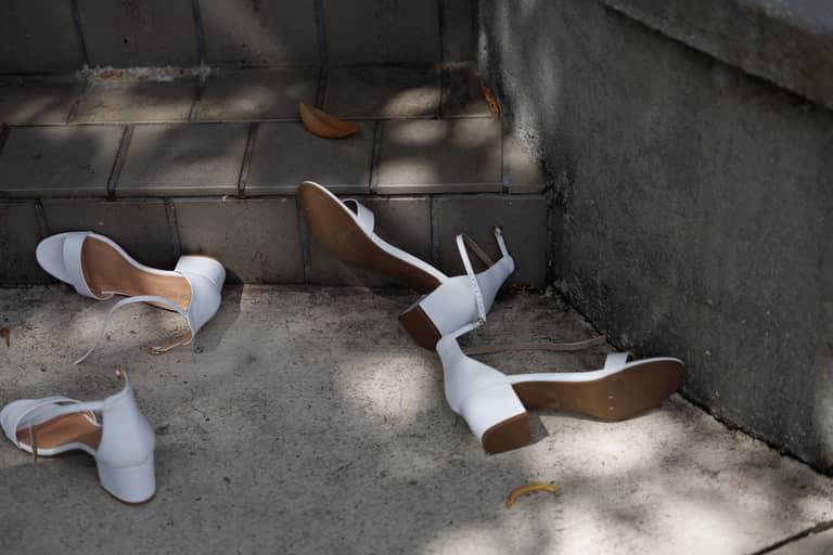White wedding heels lie scattered on concrete steps with fallen leaves