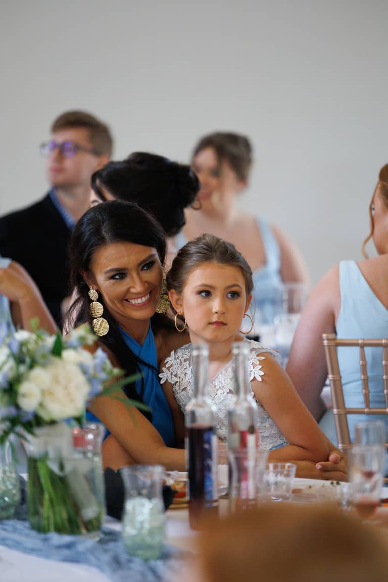 A smiling woman and a young girl sit at a wedding reception table