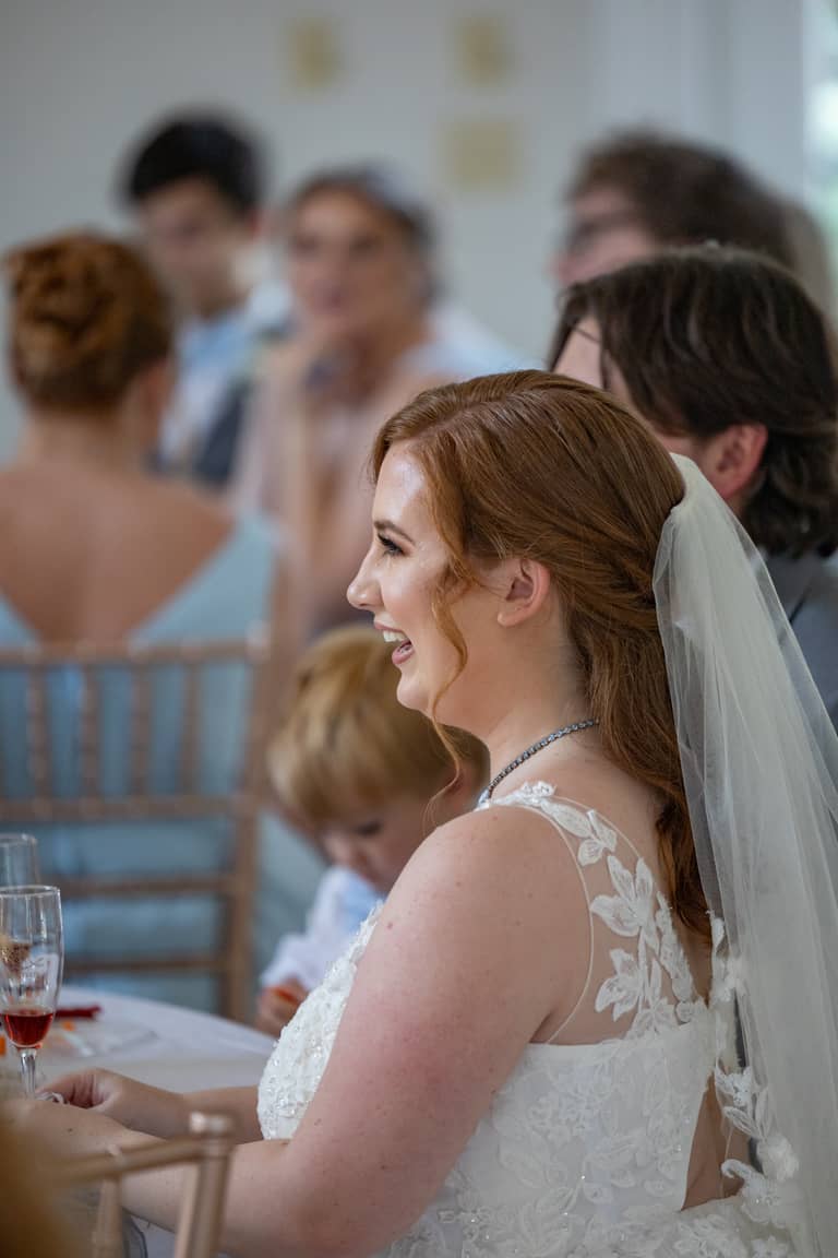 Bride laughing at a wedding reception, wearing a white lace dress and veil