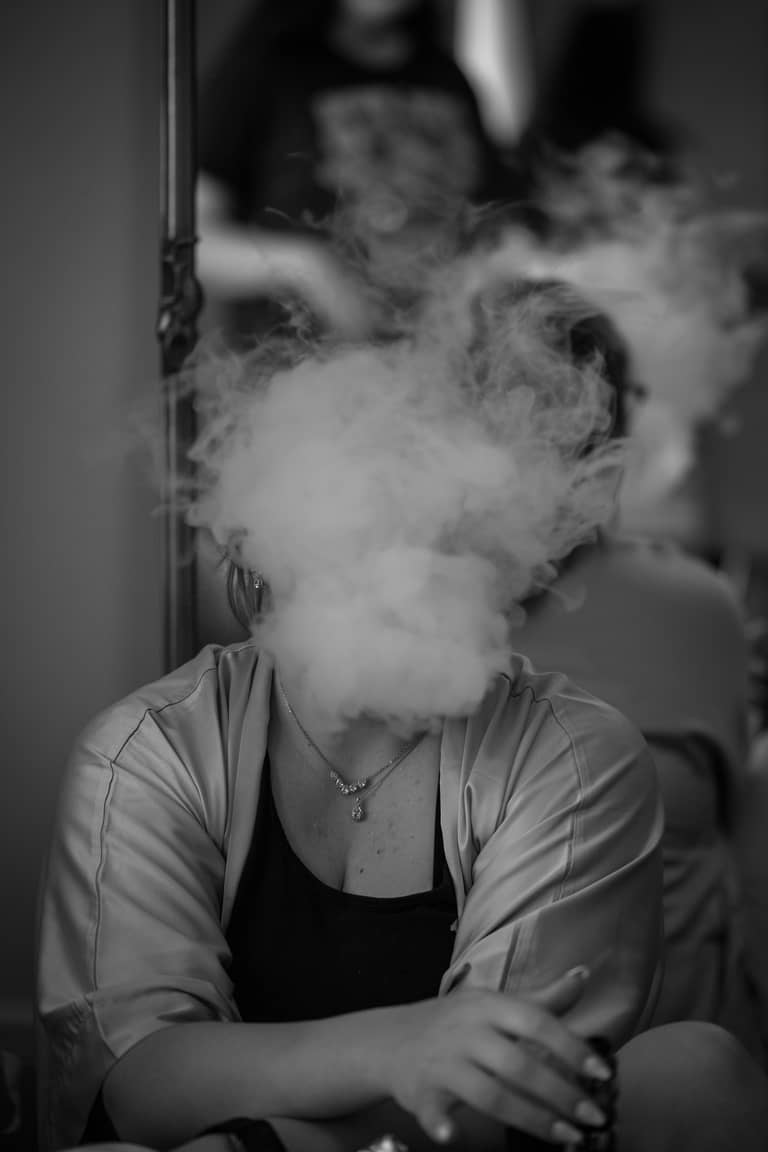 Bride in robe exhales smoke in a dramatic black and white wedding portrait