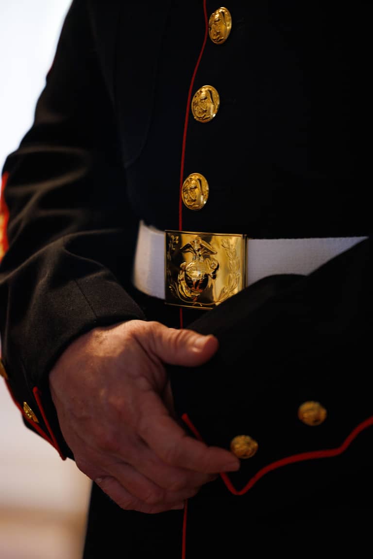 Close-up of a groom in a formal military uniform with gold buttons and belt buckle