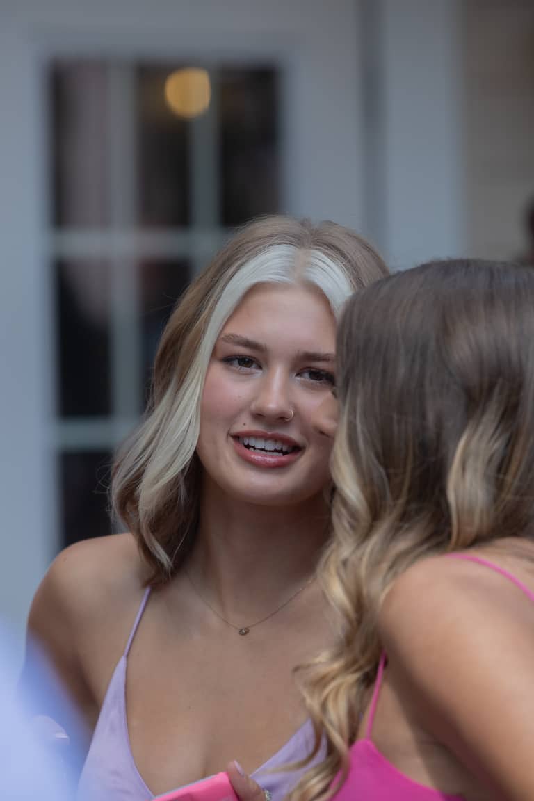 A young woman with blonde streaks smiles at a wedding reception outdoors