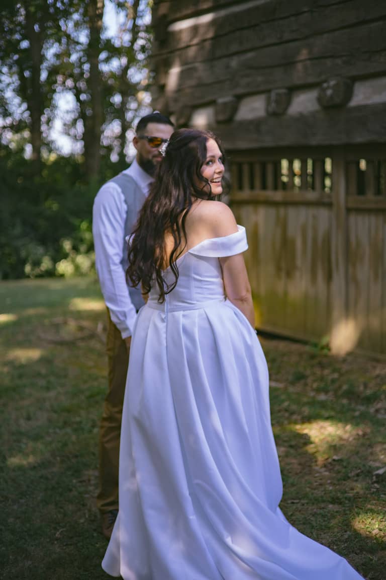 Bride and groom pose outdoors near a wooden structure during their wedding day
