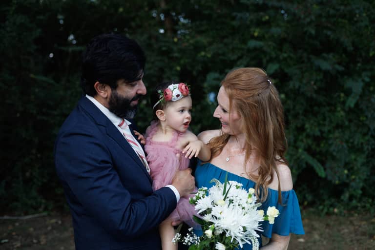 Wedding portrait of a couple holding their baby daughter outdoors with a floral bouquet