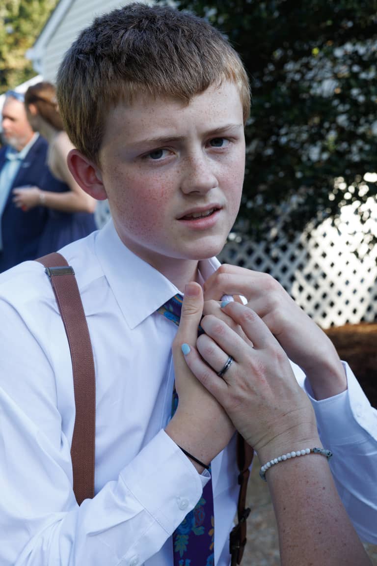 Young boy with freckles adjusts his tie during a wedding ceremony outdoors