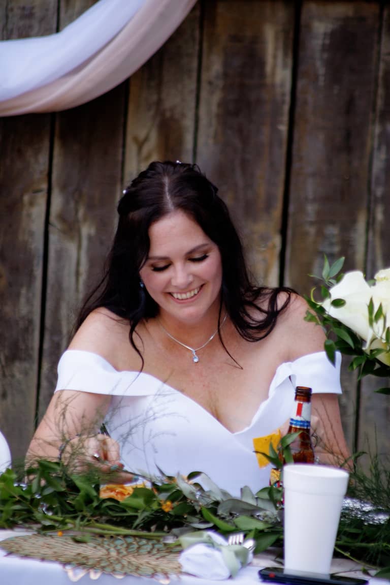 Bride smiling at her wedding reception table with floral arrangements and drinks