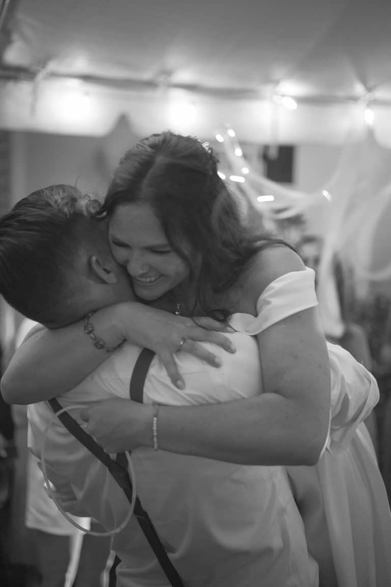 Joyful bride hugs groom tightly at their wedding reception with string lights above