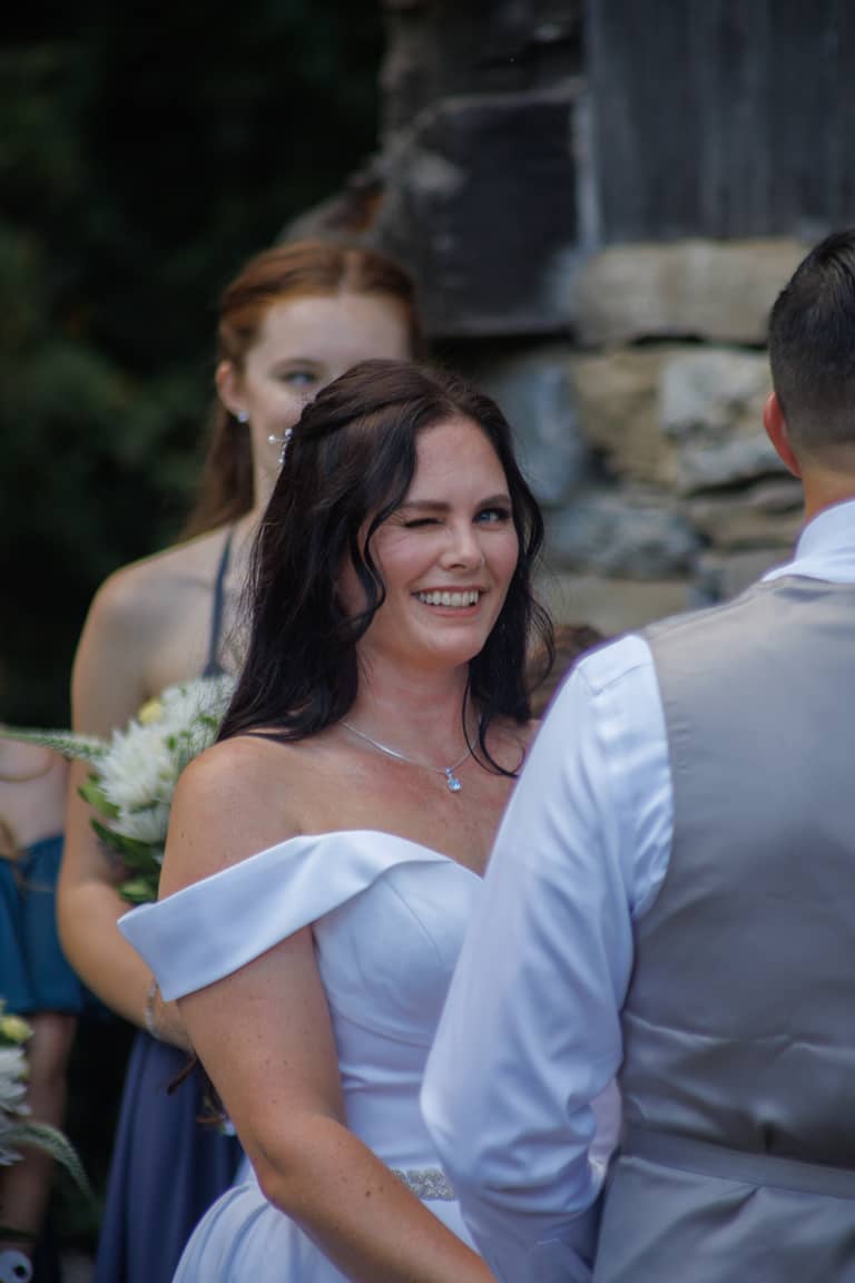 Bride winks playfully during an outdoor wedding ceremony with a stone background