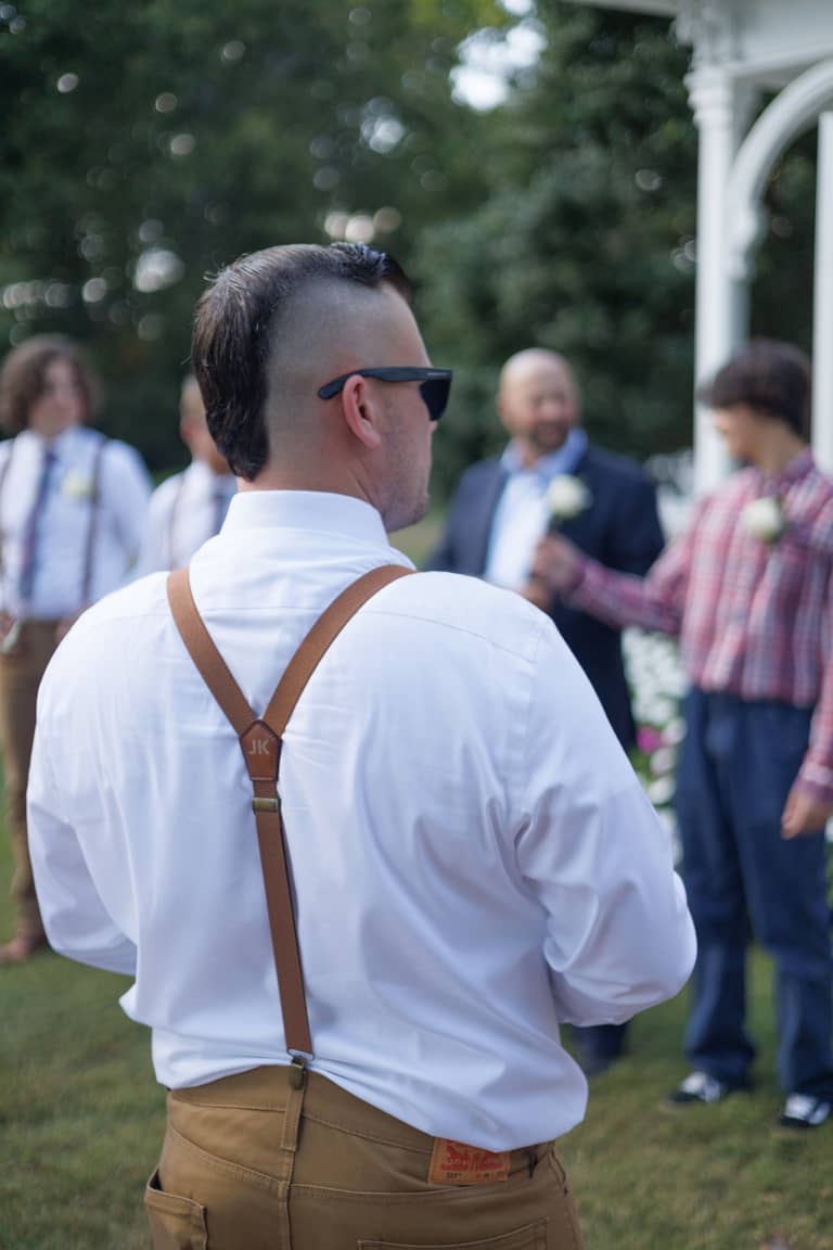 Groom with mohawk and suspenders at an outdoor wedding ceremony