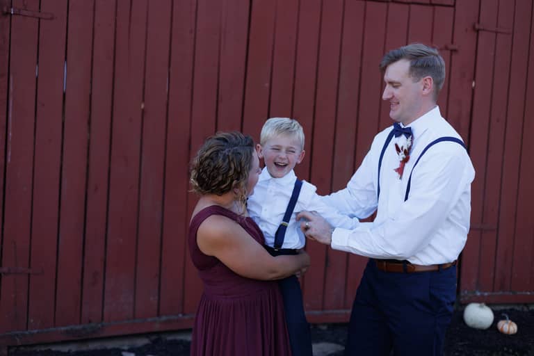 Joyful wedding party members laugh together in front of a rustic red barn