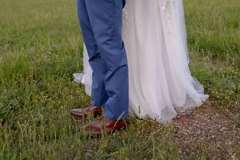 Groom's blue suit and bride's white dress stand in a grassy field