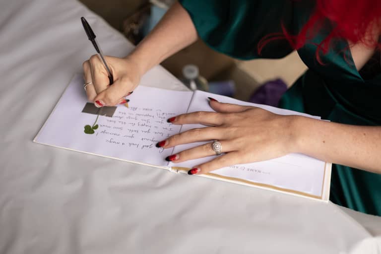 Bride writes a heartfelt message in a wedding guest book with a four-leaf clover