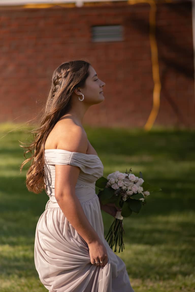 A bridesmaid in a light gown holds a bouquet while walking outdoors