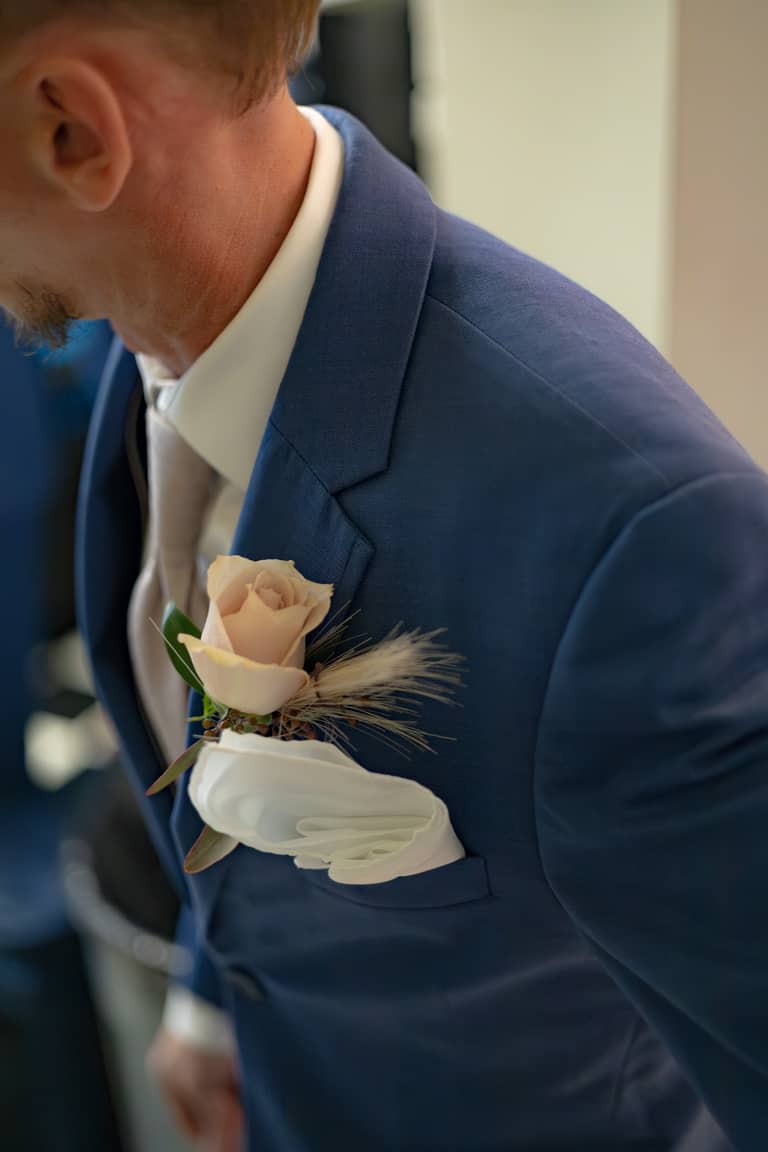 Groom's navy suit lapel with a delicate rose boutonniere and pocket square at a wedding
