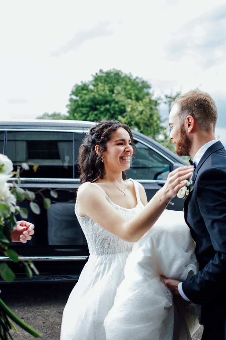 Joyful bride and groom share a moment by a car during their wedding day celebration